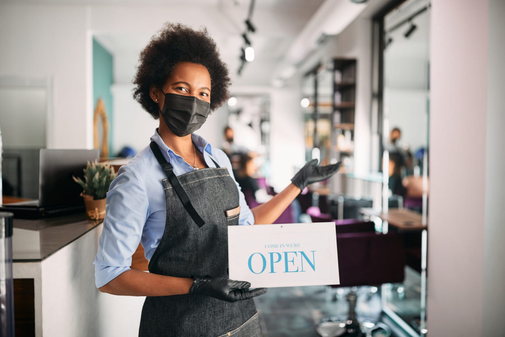 Employee holding "Open" sign in salon.