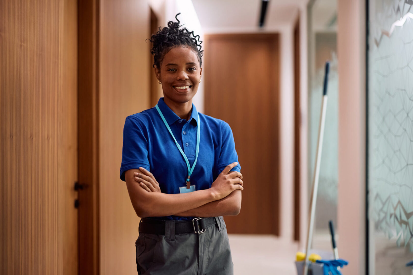 Happy African American professional cleaner standing with her arms crossed and looking at camera.
